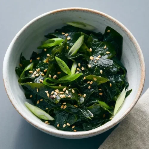 Chilled seaweed salad with a glossy sesame miso dressing and toasted white sesame seeds in a dark ceramic bowl.