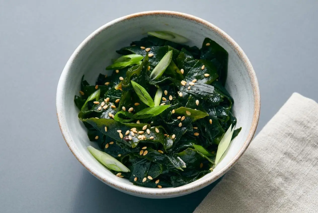Chilled seaweed salad with a glossy sesame miso dressing and toasted white sesame seeds in a dark ceramic bowl.