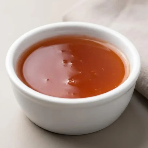 A bowl of glossy, vibrant red sweet and sour sauce showing a smooth, reflective texture.