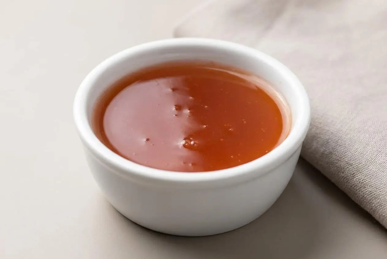 A bowl of glossy, vibrant red sweet and sour sauce showing a smooth, reflective texture.