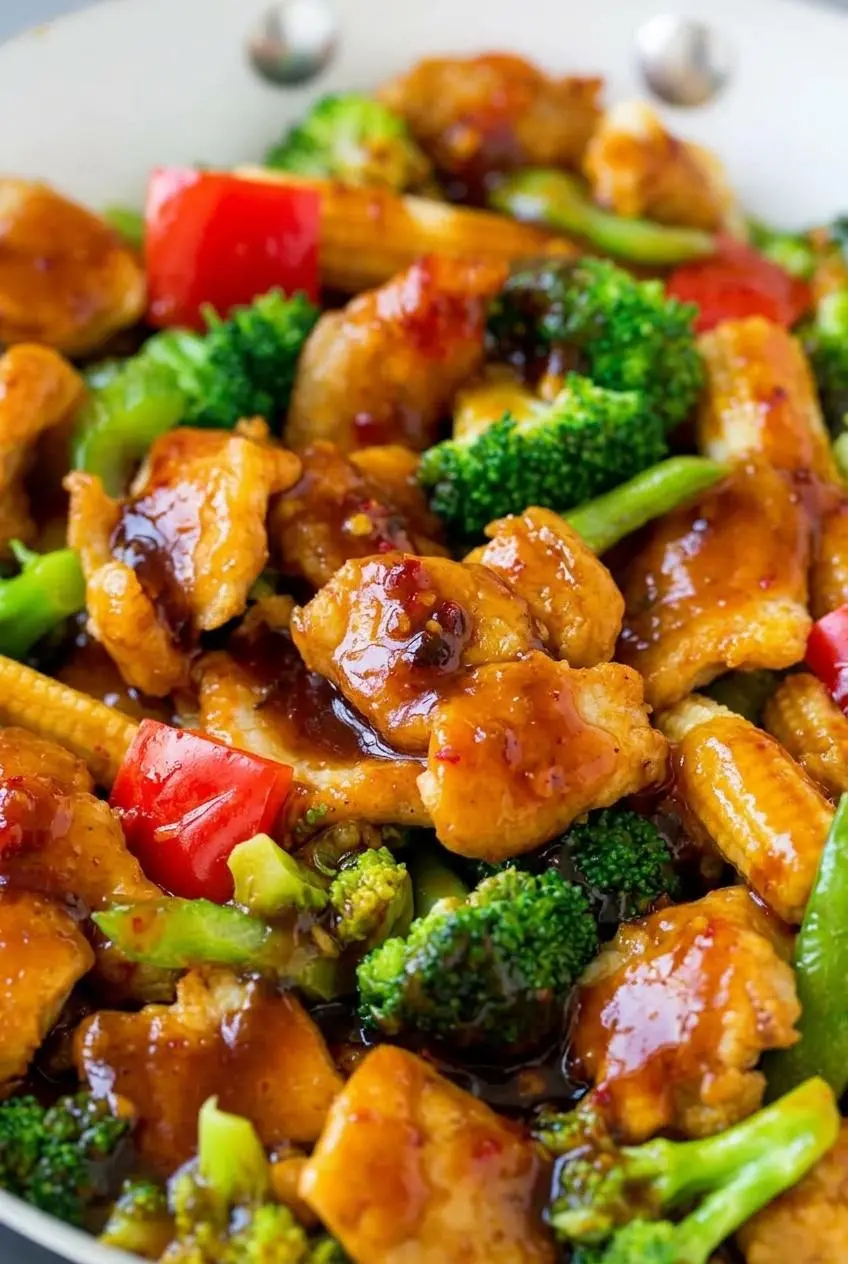 Close-up of seared Hunan chicken slices with glossy chili garlic sauce and crisp broccoli florets.