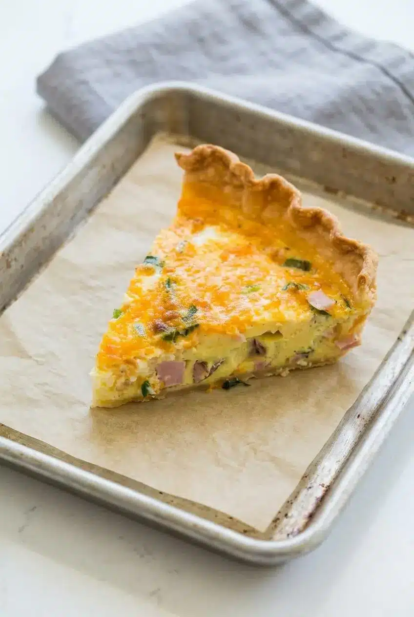 Leftover quiche slice on a parchment-lined baking sheet ready to reheat in the oven.