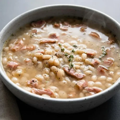 Bowl of hearty navy bean soup with tender white beans, shredded smoky ham, and fresh herbs in rich broth.