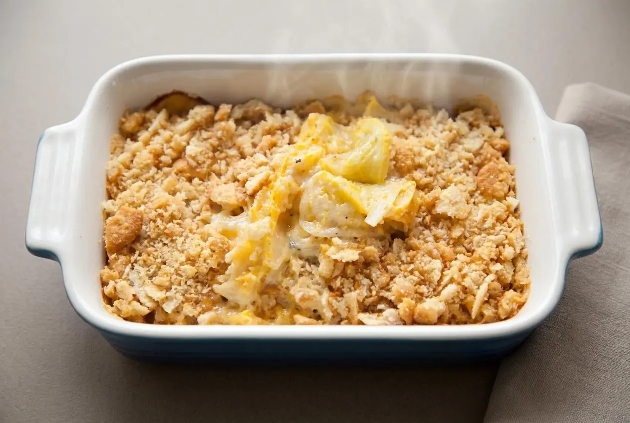 A baked yellow squash casserole recipe featuring a golden, bubbly cheese edge and a crisp cracker topping.