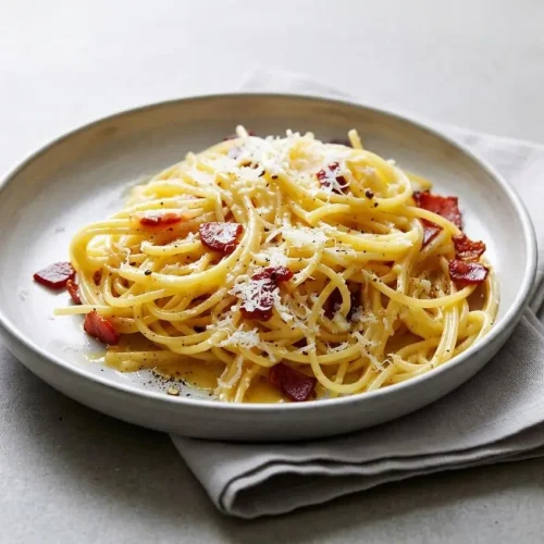 Spaghetti carbonara recipe with glossy egg sauce, crisp guanciale lardons, and freshly cracked black pepper.