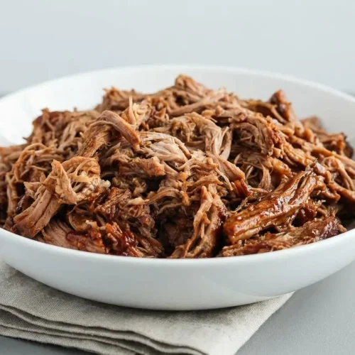Tender Crock Pot Pulled Pork shreds coated in glossy barbecue sauce with caramelized edges.