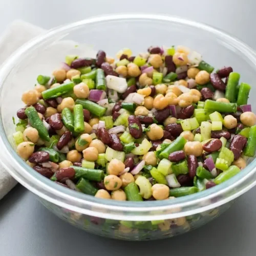 A vibrant three bean salad recipe featuring dark kidney beans, chickpeas, and green beans with a glossy dressing.