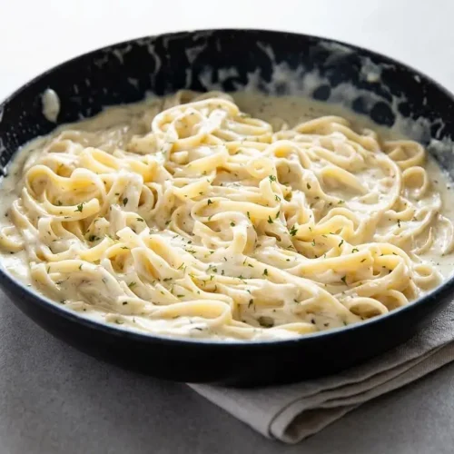 Rich and glossy homemade alfredo sauce recipe with fresh parmesan and heavy cream in a skillet.