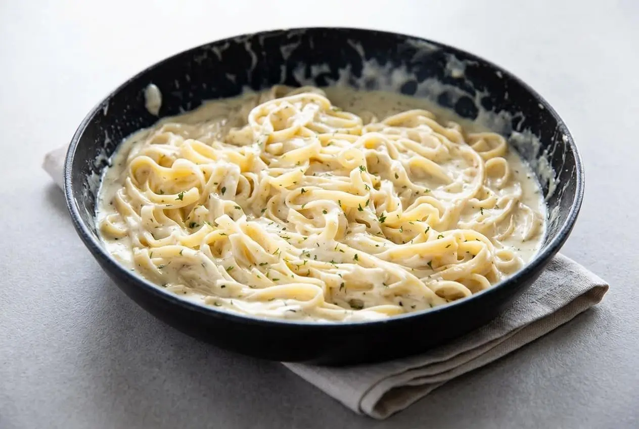 Rich and glossy homemade alfredo sauce recipe with fresh parmesan and heavy cream in a skillet.