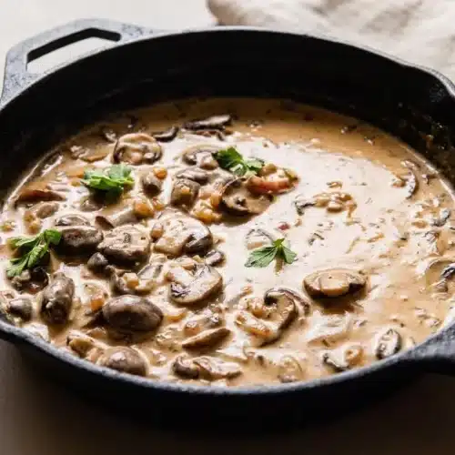 Creamy marsala sauce with golden browned mushrooms and rosemary in a skillet with a glossy finish