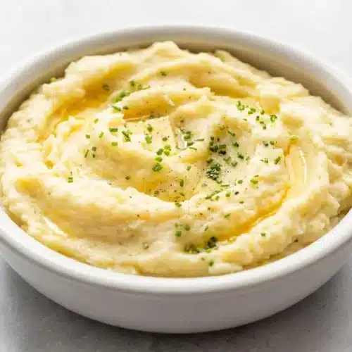 Creamy and fluffy Yukon Gold mashed potatoes in a bowl, topped with melted butter and chopped chives.