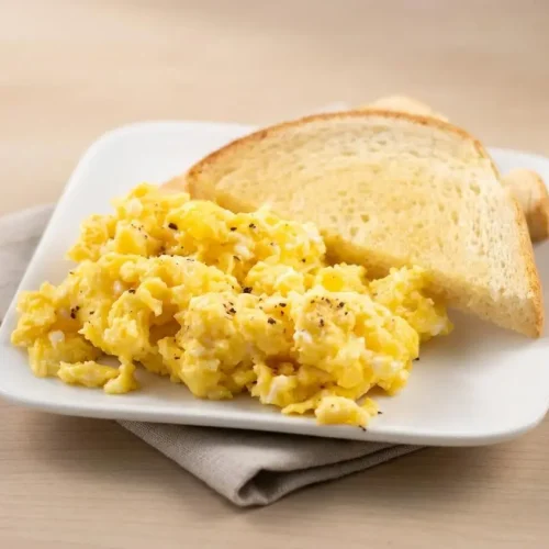 Baked scrambled eggs in a baking dish featuring soft, fluffy golden curds with a moist sheen.