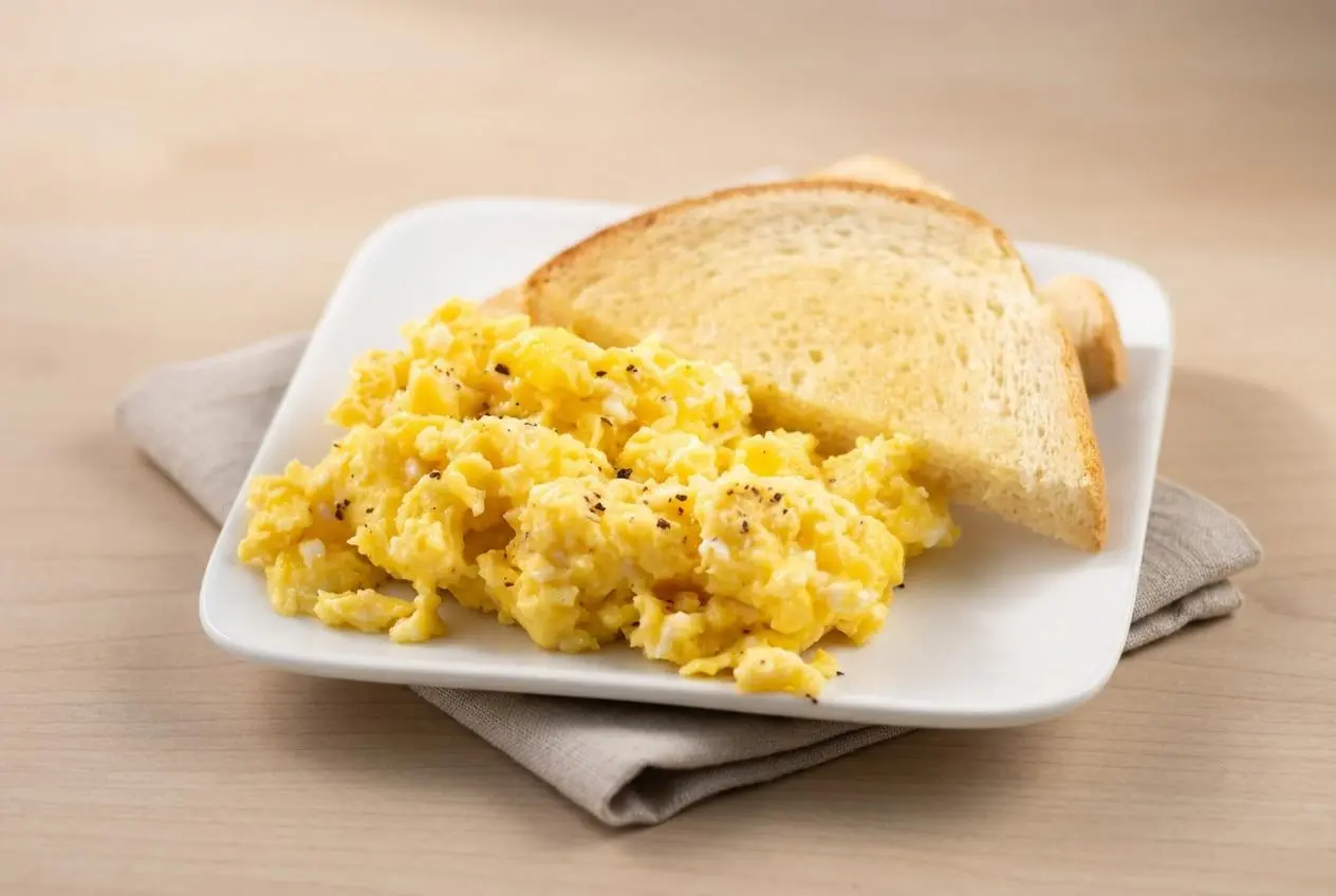 Baked scrambled eggs in a baking dish featuring soft, fluffy golden curds with a moist sheen.
