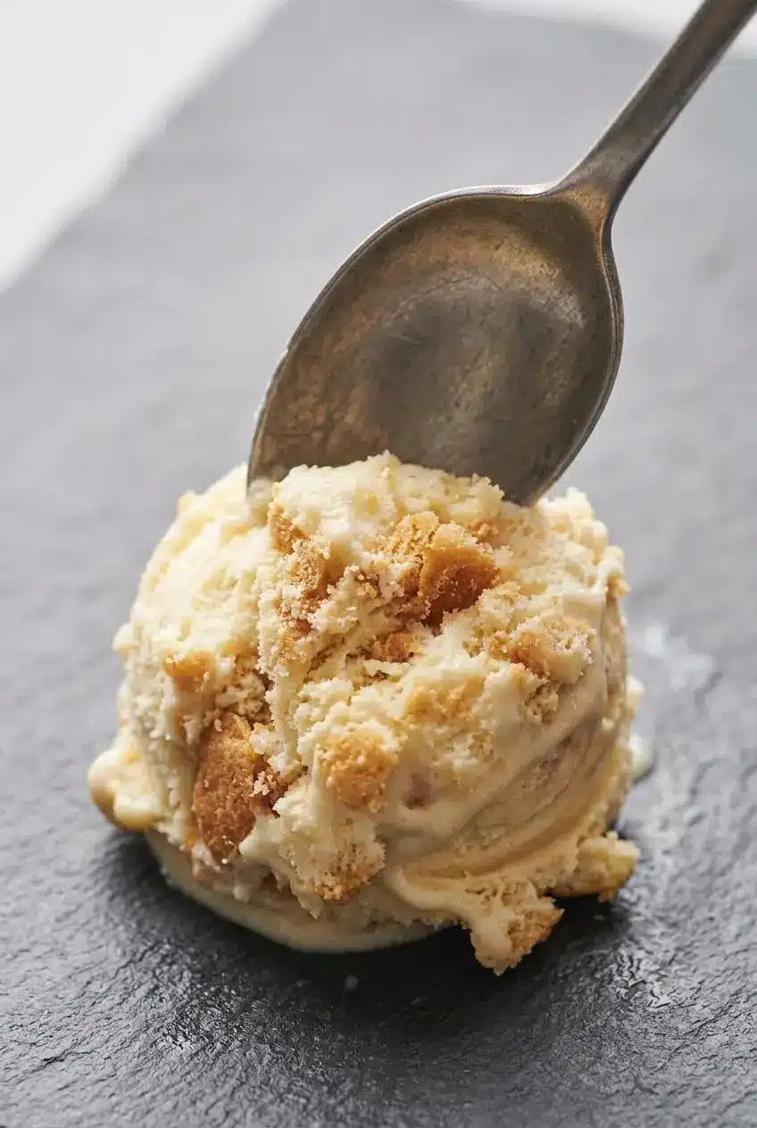 Macro close-up of a metal spoon carving a velvety scoop of no-churn banana pudding ice cream.