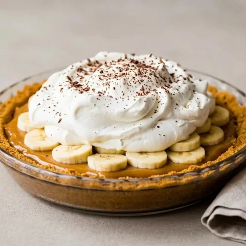 Banoffee pie topped with billowy vanilla whipped cream and dark chocolate curls in a pie dish.