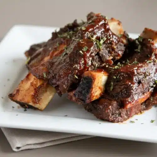 Glazed beef ribs recipe featuring tender meat and a glossy, caramelized barbecue sauce crust on a serving board.