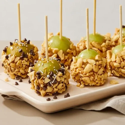 Caramel apple grapes coated in warm melted caramel and chopped peanuts on toothpicks.