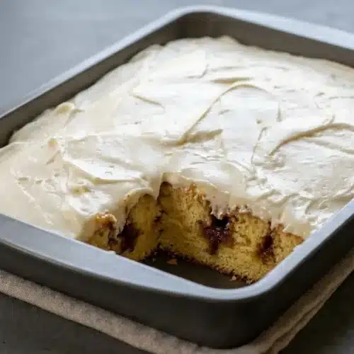 Frosted slice of cinnamon roll poke cake showing gooey brown sugar channels and creamy cream cheese frosting.