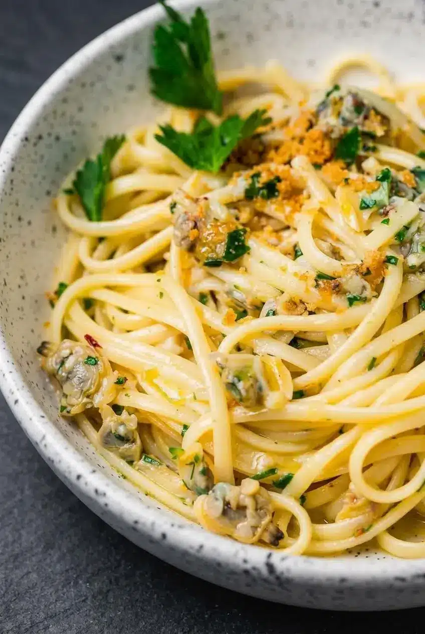 Close-up of glossy clam sauce emulsified with starchy pasta water coating linguine strands and baby clams.