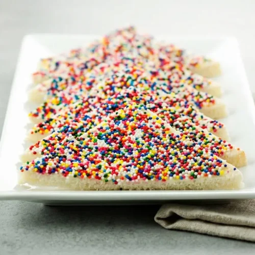 Fairy bread sliced into neat party triangles covered in colorful crunchy nonpareils and smooth butter.