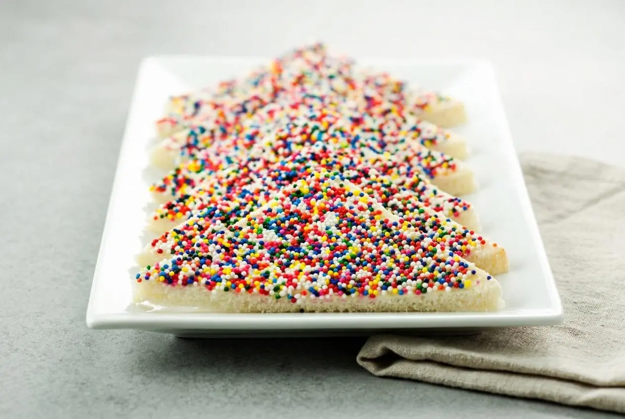 Fairy bread sliced into neat party triangles covered in colorful crunchy nonpareils and smooth butter.