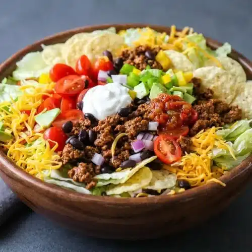 Classic taco salad recipe layered with savory seasoned ground beef, cheddar, creamy avocado, and crunchy tortilla chips.