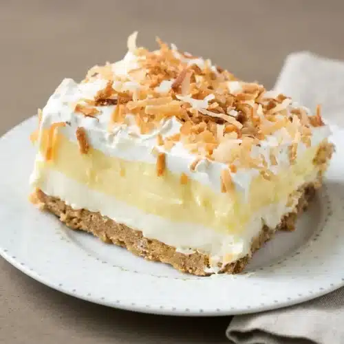 Chilled coconut cream lush square with creamy pudding layers and toasted coconut flakes on top.