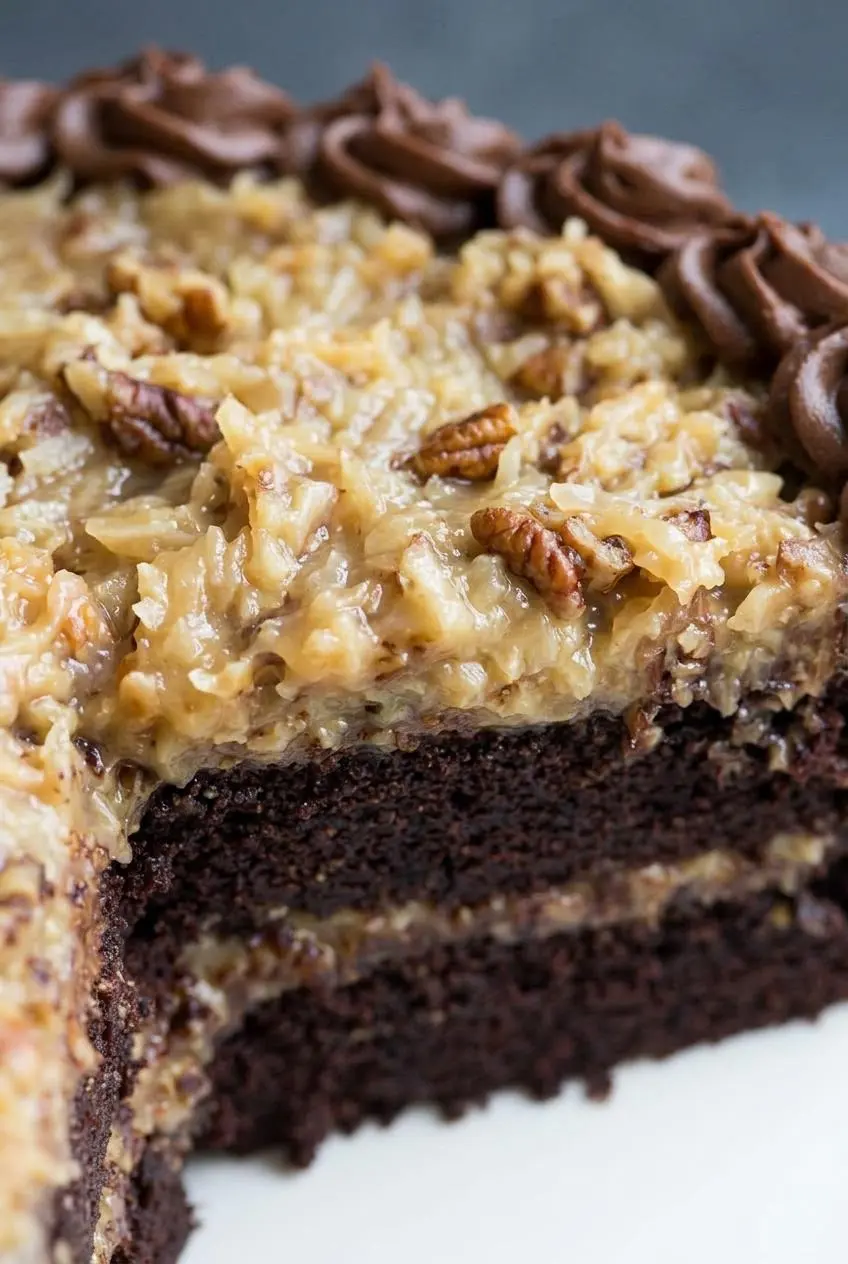 Macro view of gooey coconut pecan custard filling loaded with toasted nuts over chocolate cake.