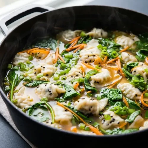 Dumpling soup in savory broth with tender potstickers, julienned carrots, and glossy sesame oil droplets.
