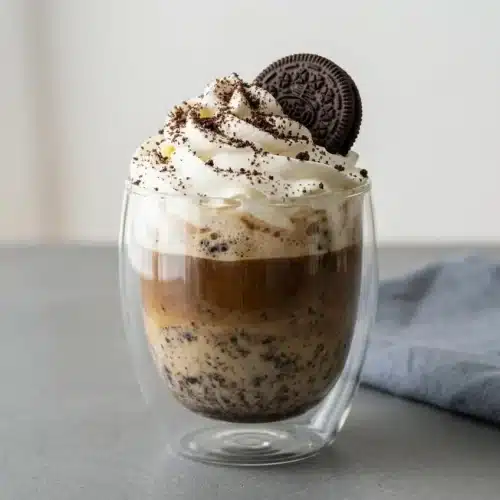 Warm cookies and cream latte topped with velvety whipped cream and chocolate cookie crumbs in a glass mug.