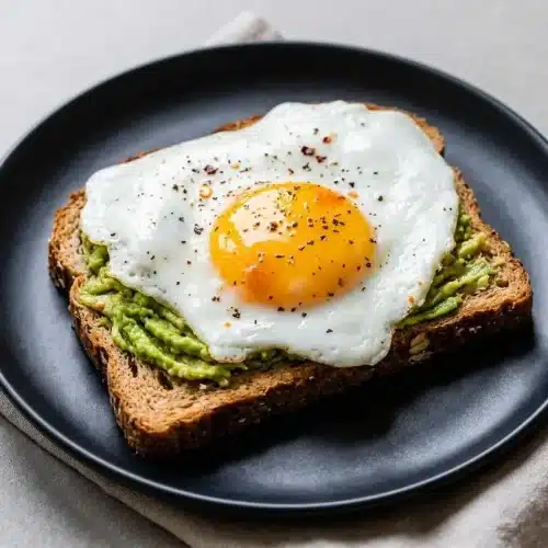 Avocado toast with egg on crisp sourdough bread topped with black pepper and olive oil drizzle.