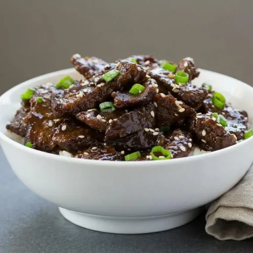 Beef teriyaki recipe featuring crisp-edged flank steak coated in a glossy garlic ginger glaze with sliced scallions.