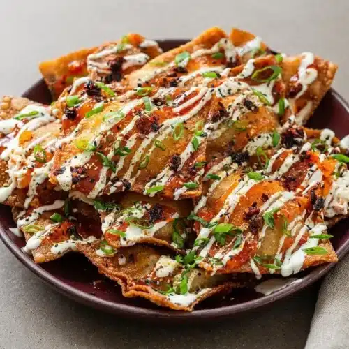Crab rangoon nachos with blistered golden wontons, creamy crab filling, sweet chili drizzle, and scallions.