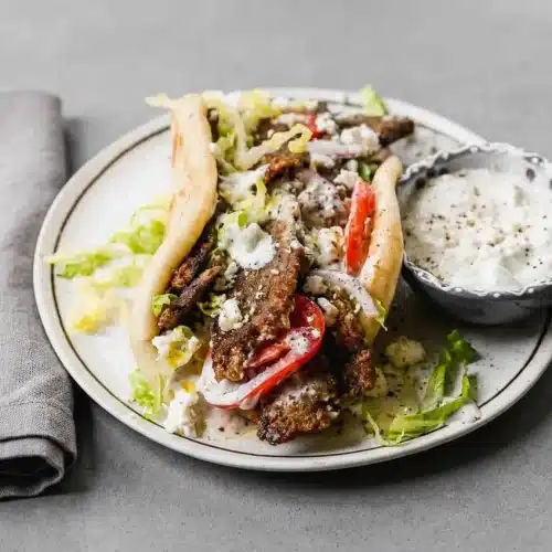 Lamb gyros tucked into warm pita bread with crisp seared meat strips, cool tzatziki, and sliced tomatoes.