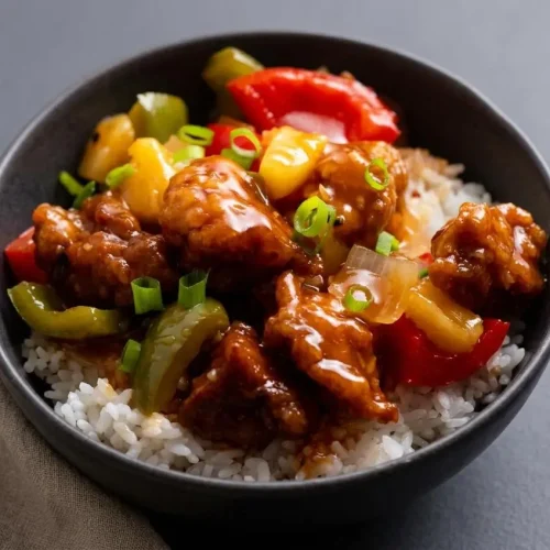Crispy sweet and sour pork recipe tossed with pineapple and bell peppers in a glossy red glaze.