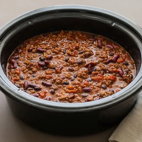 Crockpot chili recipe in a rustic bowl featuring hearty ground beef, kidney beans, and a rich, glossy brick-red sauce.