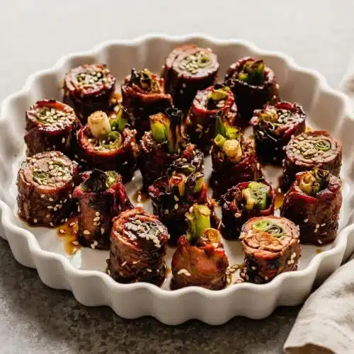 Platter of sliced beef negimaki rolls filled with crisp scallions and coated in a glossy, dark soy mirin glaze.