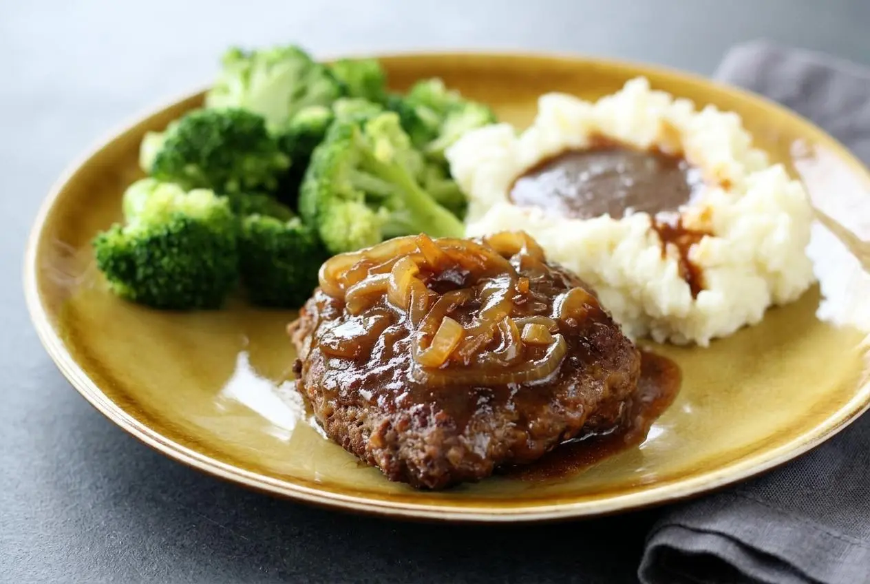 Hamburger steak recipe patties simmering in glossy brown onion gravy in a skillet.