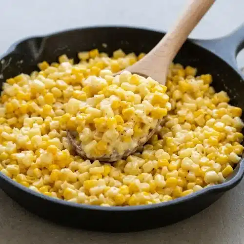 Honey butter skillet corn coated in a rich, glossy cream cheese glaze with cracked black pepper.
