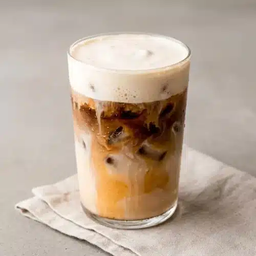 Iced carrot cake latte in a tall glass topped with a silky, pourable layer of cream cheese cold foam.