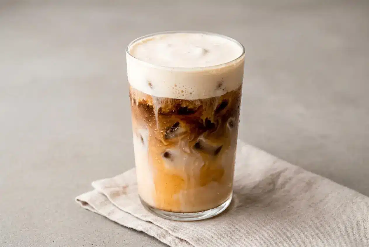 Iced carrot cake latte in a tall glass topped with a silky, pourable layer of cream cheese cold foam.