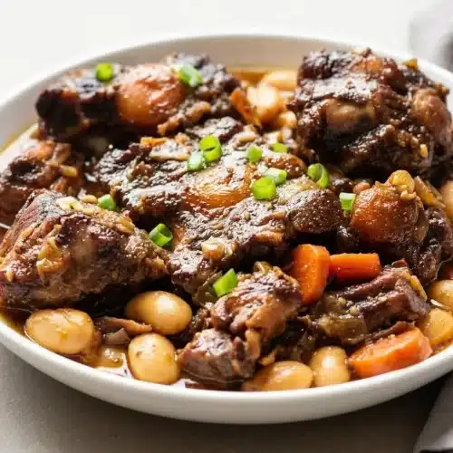 Tender Jamaican oxtail recipe braised in glossy mahogany gravy with creamy butter beans and sliced carrots.