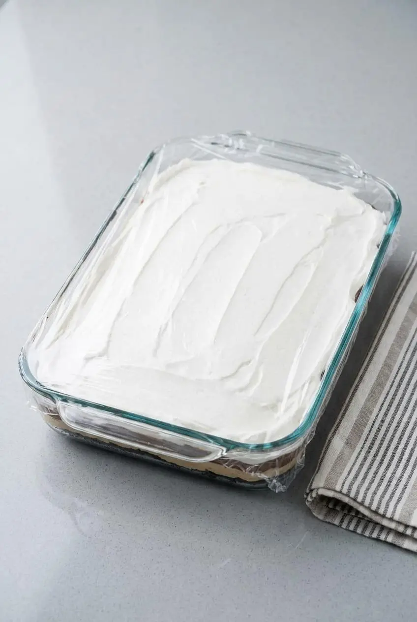 A 9x13 glass pan of layered dessert covered tightly in plastic wrap for refrigerator chilling.
