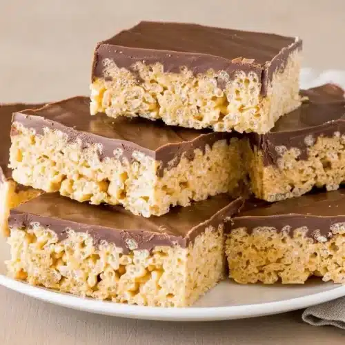 Peanut butter rice krispie treats topped with a smooth, glossy chocolate layer.