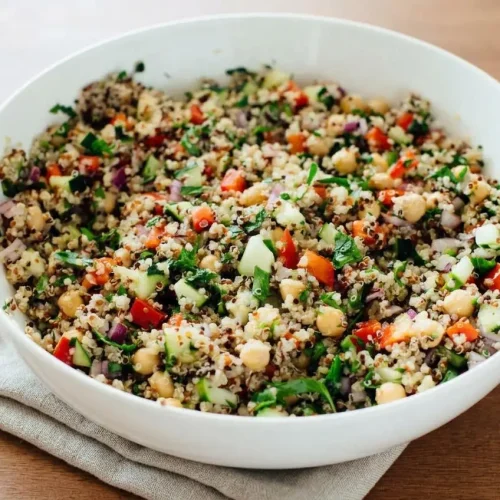 Quinoa salad recipe in a ceramic bowl with crisp vegetables, chickpeas, and a bright glossy lemon dressing.