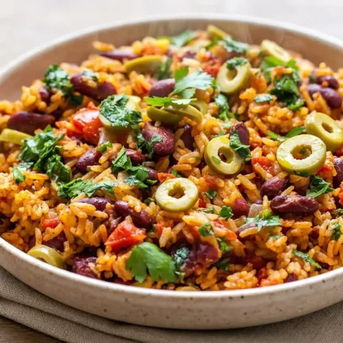 Rice and beans recipe in a skillet topped with tender kidney beans, sliced olives, and glossy green parsley oil.