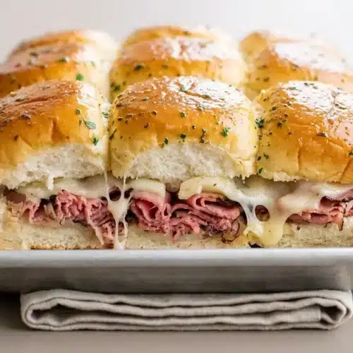Baked roast beef sliders on sweet rolls with melted provolone cheese and a glossy garlic butter crust.