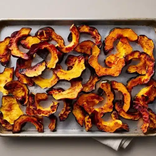 Roasted acorn squash crescent slices with deeply caramelized golden edges and tender orange flesh on a platter.