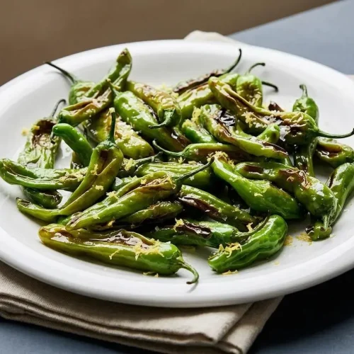 Finished shishito peppers recipe with charred blistered skins, flaky sea salt, and fresh lemon zest.