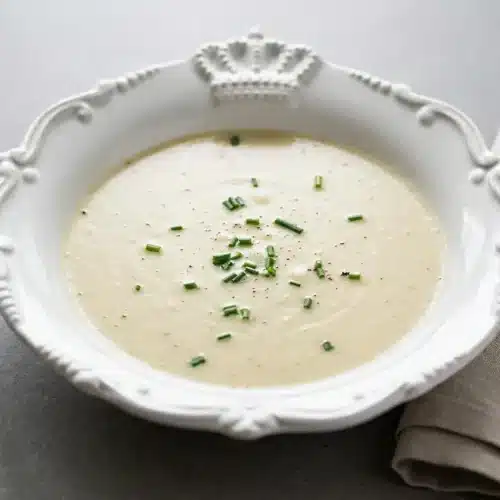 Chilled vichyssoise soup in a ceramic bowl garnished with fresh minced chives and a glossy cream finish.